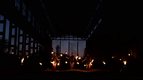 Four-women-in-leather-clothes-with-fire-dance-and-show-fire-show-a-man-with-a-flamethrower-in-the-back-plays-with-the-flame-in-slow-motion